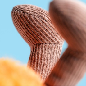 Jellycat plush toy close-up detail showing brown ribbed textured surface with multi-coloured elements on blue background