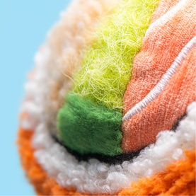 Jellycat plush toy close-up showing multicoloured textured layers in orange, green, yellow and white, resembling a sushi roll design.