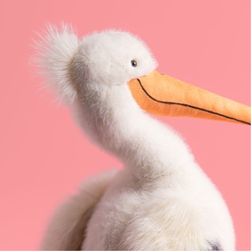 Jellycat white plush pelican soft toy with fluffy feather texture, orange beak, and pink background. Close-up detail shot.