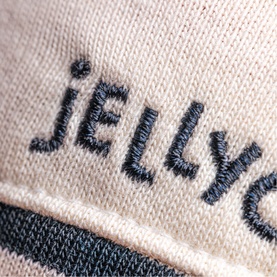 Jellycat plush toy close-up showing embroidered navy logo on cream fabric with navy stripe detail