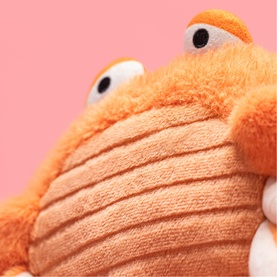 Jellycat orange fluffy plush toy with ridged texture, googly eyes and fuzzy top, close-up detail shot