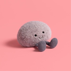 Jellycat small grey pebble-shaped soft toy with embroidered smile and stubby legs, against pink background