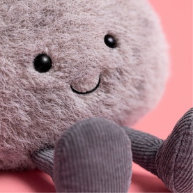 Jellycat fluffy round plush soft toy in mauve grey with corduroy limbs and embroidered smiley face, close-up detail shot
