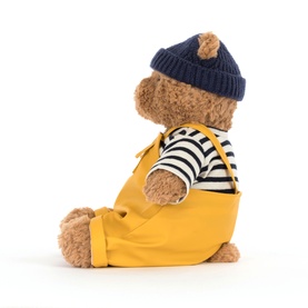 Jellycat teddy bear soft toy in golden yellow dungarees, navy striped top and knitted beanie hat, seated side profile view
