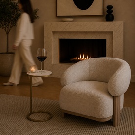 Mindy Browne Oscar Round Side Table in gold and white marble, styled beside a boucl&eacute; armchair near a lit fireplace with a candle and wine glass on