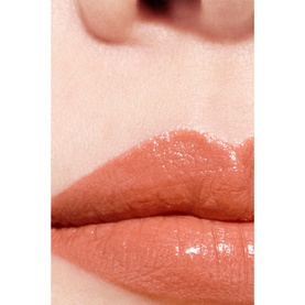 Close-up of lips wearing a glossy warm nude-peach lip colour with a sheer, hydrated finish