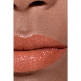 Close-up of lips wearing a warm peachy-nude glossy lipstick finish on medium skin tone