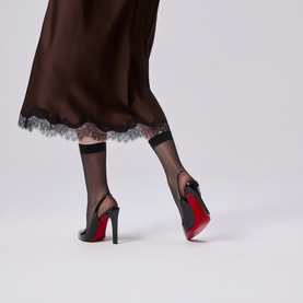Model wearing Christian Louboutin black pointed-toe stiletto heels with signature red sole, styled with sheer black socks and lace-hem satin skirt.
