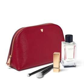 Aspinal of London Cherry Red leather cosmetic case with gold zip, styled with fragrance, lipstick, and makeup brush.