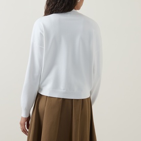 Model wearing Ted Baker Neslie Applique Rose Cardigan in ivory, back view, with khaki pleated midi skirt