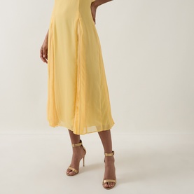 Model wearing Ted Baker Rueva Flared Dress in yellow, showing pleated midi skirt with flared silhouette, styled with gold strappy heels.