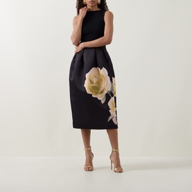 Model wearing Ted Baker Verinie Placement Floral Dress in black, midi length with large floral print skirt, boat neck, styled with gold heeled sandals
