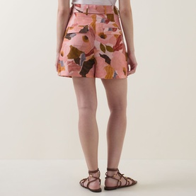 Model wearing Ted Baker Noysa Floral Print Shorts in coral with abstract floral print, styled with brown lace-up flat sandals, rear view.