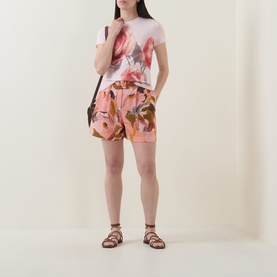 Model wearing Ted Baker Noysa Floral Print Shorts in coral with a floral print tee, styled with brown leather sandals and a dark shoulder bag.