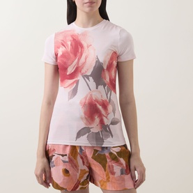 Model wearing Ted Baker Bindii Placement Floral T-Shirt in coral with large rose print, styled with matching floral shorts.