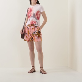 Model wearing Ted Baker Bindii Placement Floral T-Shirt in coral with matching floral shorts, small brown crossbody bag and strappy flat sandals.