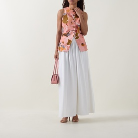 Model wearing Ted Baker Narlla Floral Print Waistcoat in coral with white wide-leg trousers, styled with a pink bag and tan sandals.