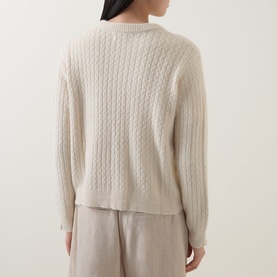 Model wearing Masai Leryntha Knit Cardigan in beige, rear view showing cable-knit texture, dropped shoulders, and ribbed trims, styled with taupe