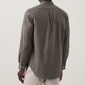Model wearing Paul Smith blue striped cotton-silk casual shirt, rear view, with curved hem and button cuffs, styled with white trousers.