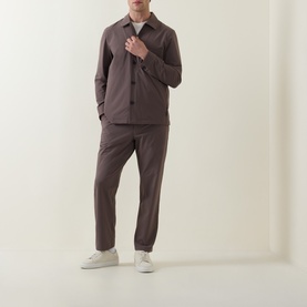 Model wearing Paul Smith grey casual trousers styled with a matching dark brown overshirt and white low-top trainers.