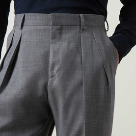 Model wearing Paul Smith Double Pleat Wool Trousers in grey, showing double-pleated front, belt loops and side pockets, styled with a navy top.