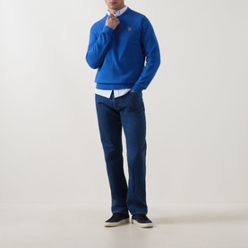 Model wearing Paul Smith blue cotton jeans styled with a cobalt crew neck jumper, white shirt and navy slip-on shoes.