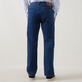 Model wearing Paul Smith blue cotton jeans, rear view, showing straight leg fit, tan leather patch detail and back pockets, styled with light blue