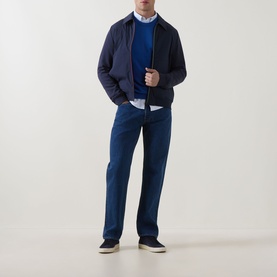 Model wearing Paul Smith blue cotton formal trousers, styled with a navy zip jacket, blue knit and white shirt, with canvas trainers.