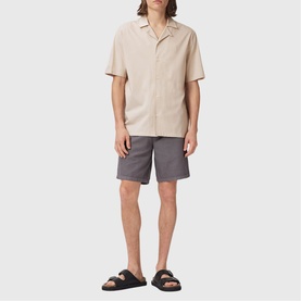 Model wearing All Saints birch white short-sleeve shirt with grey shorts and black sandals.