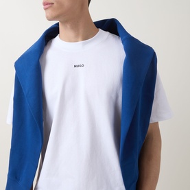 Model wearing Hugo white cotton crew neck T-shirt with small logo print, styled with a blue sweatshirt draped over shoulders.