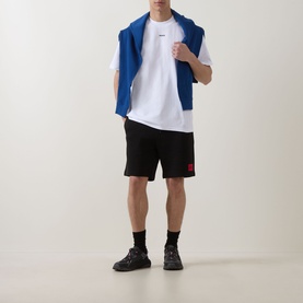 Model wearing Hugo white crew neck T-shirt with black shorts and dark trainers, blue sweatshirt draped over shoulders