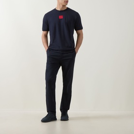 Model wearing Hugo navy crew neck T-shirt with red logo patch, styled with navy trousers and dark trainers