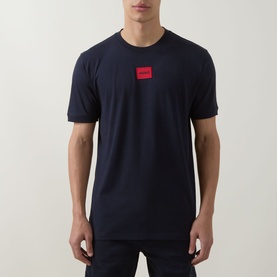 Model wearing Hugo navy crew neck T-shirt with small red logo patch on chest, paired with dark trousers