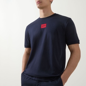 Model wearing Hugo navy cotton crew neck T-shirt with red logo patch on chest, styled with navy trousers
