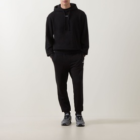 Model wearing Hugo black cotton sweatpants with elasticated cuffs, styled with matching black hoodie and dark grey trainers.
