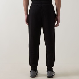 Model wearing Hugo black cotton sweatpants, shown from behind with elasticated waistband and tapered leg, styled with grey trainers.