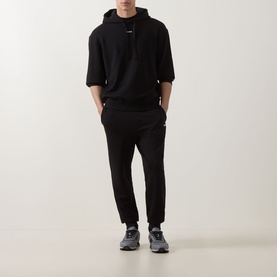 Model wearing Hugo black cotton sweatpants, styled with matching black short-sleeve hoodie and grey trainers.