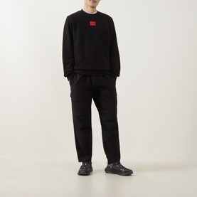 Model wearing Hugo Diragol Logo Sweatshirt in black with crew neck and red logo patch, styled with black trousers and dark trainers.