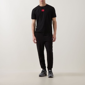 Model wearing Hugo black cotton T-shirt with red logo patch, styled with matching black joggers and grey trainers