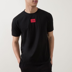 Model wearing Hugo black cotton T-shirt with red logo patch on chest, styled with black trousers