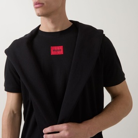 Model wearing Hugo black cotton T-shirt with red logo patch, styled with a black blazer draped over shoulders.