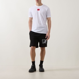 Model wearing Hugo white cotton T-shirt with red chest logo, styled with black graphic shorts and black trainers.
