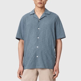 Model wearing All Saints lunar blue short-sleeve camp collar shirt, styled with stone chino trousers.