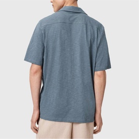Model wearing All Saints lunar blue short-sleeve camp collar shirt, back view, styled with stone chinos.