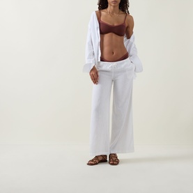 Model with Tala Deep Rust bikini top, styled with white wide-leg trousers, open shirt and tan sandals.