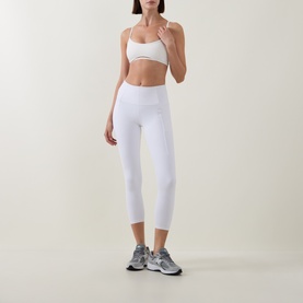 Model wearing Tala DayFlex Strappy Back Sports Bra in Ivory with cross-back straps, styled with white cropped leggings and grey trainers.