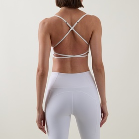 Model wearing Tala DayFlex Strappy Back Sports Bra in Ivory, showing cross-back strap detail, styled with matching white leggings.