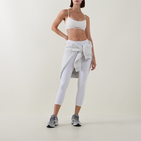 Model wearing Tala DayFlex Strappy Back Sports Bra in Ivory with matching white cropped leggings, grey shirt tied at waist and silver trainers.