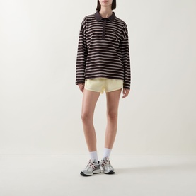 Model wearing Tala Striped Logo Rugby Top in Mocha Brown with polo collar, styled with yellow shorts and chunky trainers.