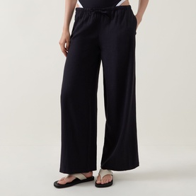 Model wearing Tala Resort Drawstring Flared Trousers in Shadow Black, with drawstring waistband and wide-leg silhouette, styled with black sandals.